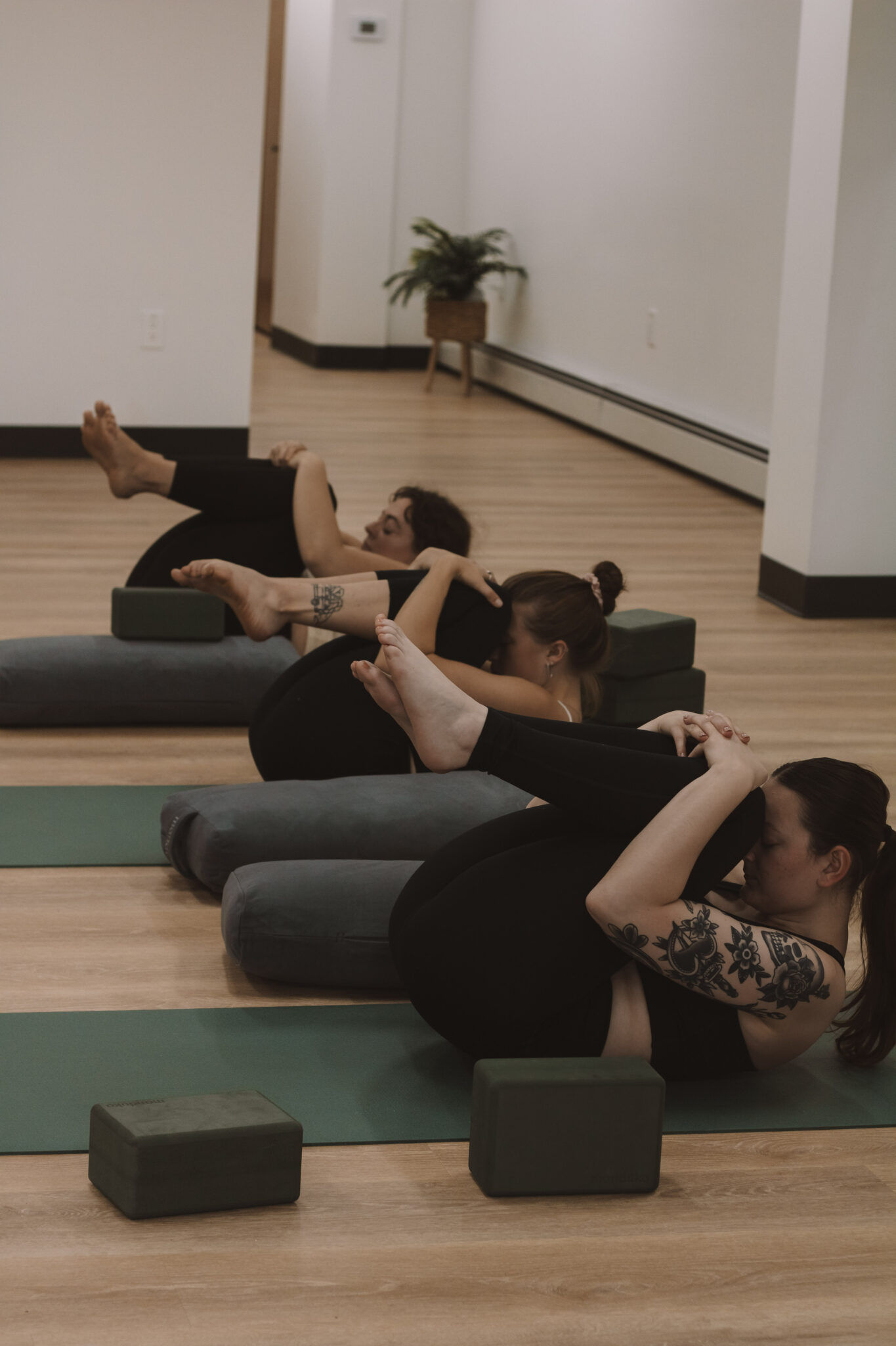 Three yoga students in seed pose at the end of their practice.